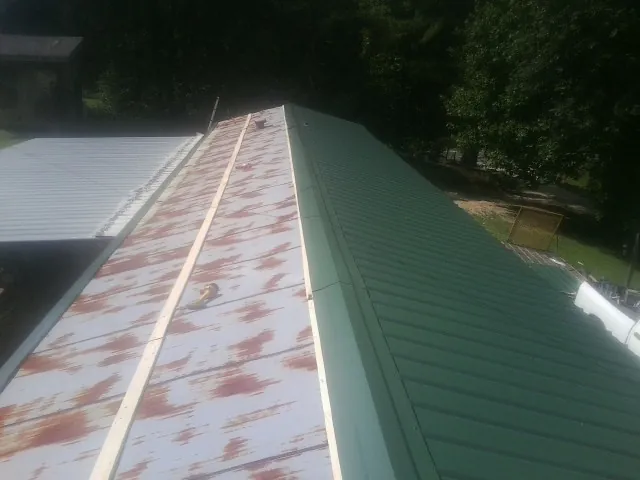 Old rusted panels beside newly installed green metal roofing — Wind Damage Roof Repair by Roofing Brothers in Pinehurst