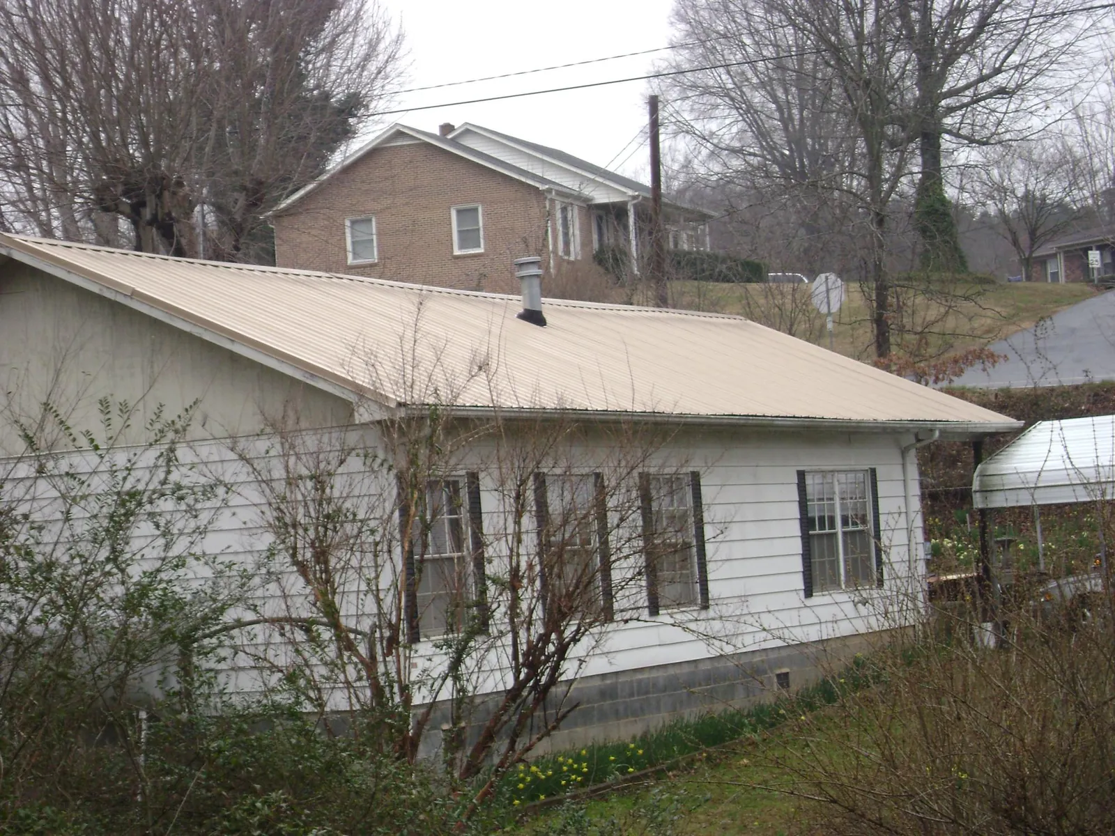 Tan metal roof on a white sided house set into a hillside — Commercial Roofing by Roofing Brothers in Pinehurst